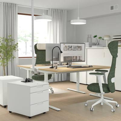 Modern home office with MITTZON adjustable desk, green chair, and white storage. Light wood top, white frame, spacious, with monitor and accessories.
