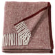 Displays a MOALIE throw blanket folded in red-brown hues made of 100% wool with a white geometric fringe pattern.