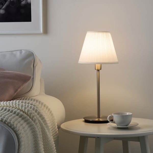 Cosy corner with MYRHULT lamp, cup, and a warm chair. Alternative: MYRHULT lamp in cosy nook with cup and warm chair.