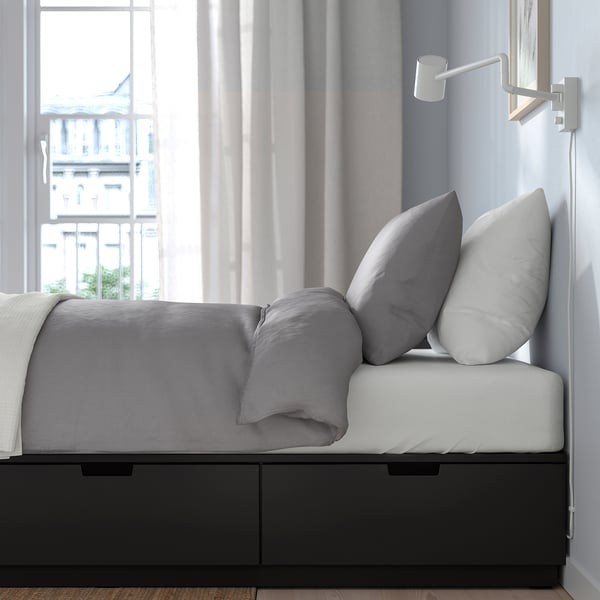 Bed with NORDLI frame, featuring drawers and wall lamp, offering storage and reading light.