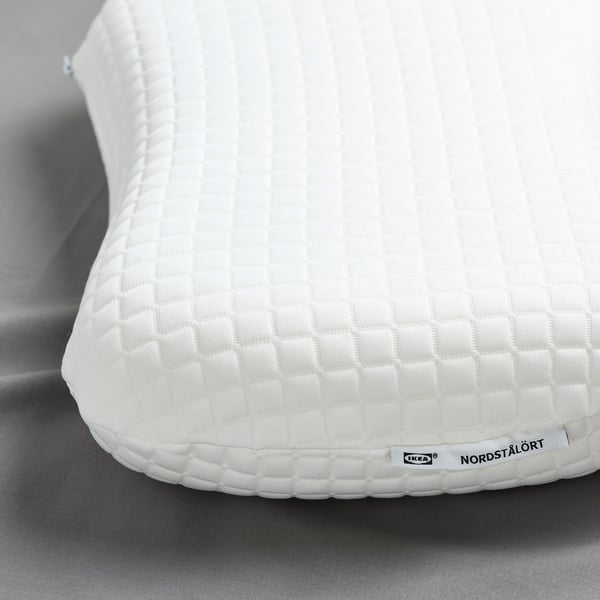 Close-up of IKEAs white ergonomic pillow for back/side sleepers, featuring textured cover and soft foam.