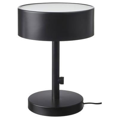 A NYMÅNE table lamp, black, with a cylindrical shade and base, made of metal and glass, providing soft diffused light.
