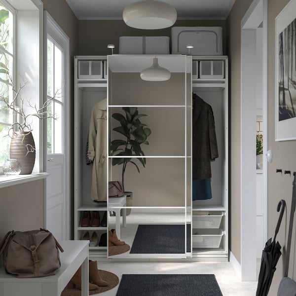 Modern closet with sliding doors, containing hangers, shelves, and a shoe rack, decorated with a beige handbag and a vase with branches.