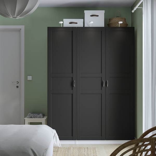 Modern bedroom with large black PAX wardrobe, white bed, green walls, and hanging wicker basket.