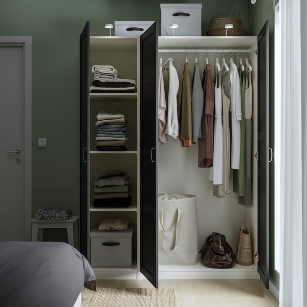 Open wardrobe displaying shelves with folded clothes and hanging garments, featuring internal storage and lighting.