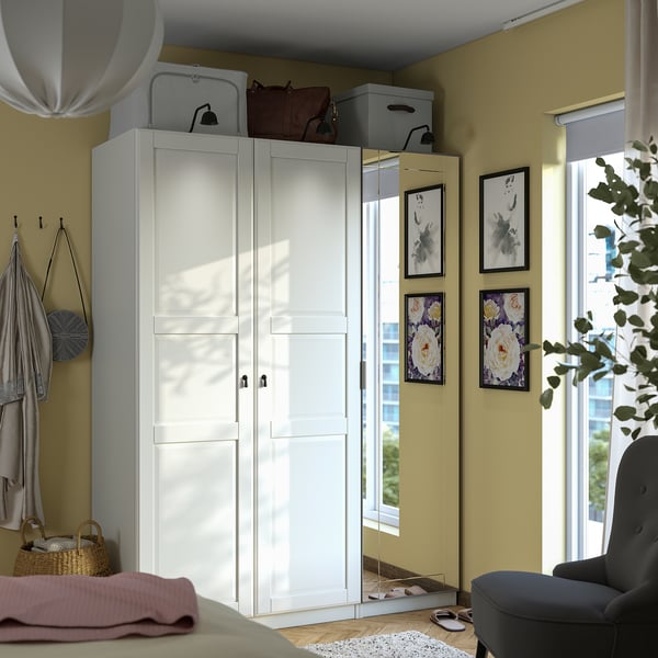 Bedroom with large white PAX wardrobe, mirrored doors, shelves, drawers, and hooks for clothes. Large window, chair, and wall decor.