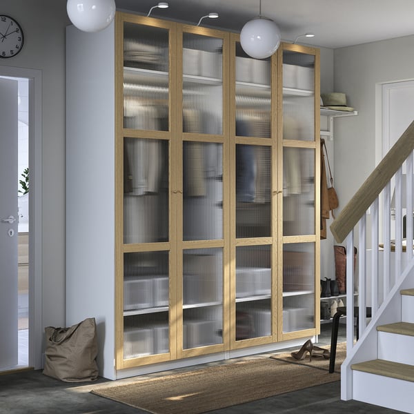 Large wooden PAX wardrobe with glass doors occupies corner, taller than nearby stairs, besides entrance; modern design.