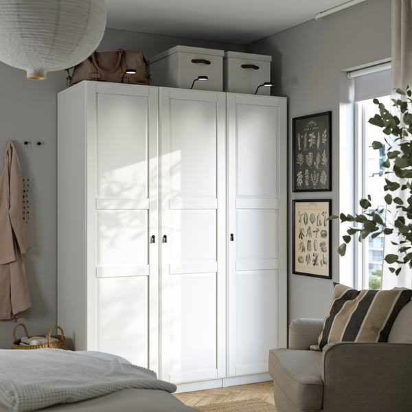 White PAX wardrobe, grey wall, beige sofa, frosted doors, grey boxes, hooks, basket, bright room, window, plant.