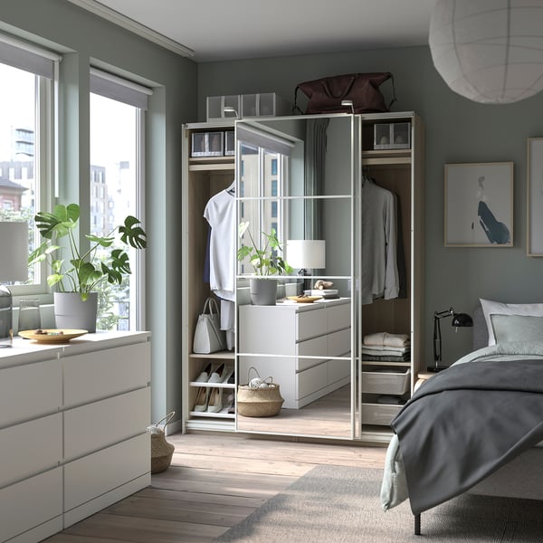 Bedroom with modern furniture: white PAX wardrobe, grey bed, wooden floor, plants, and city view.