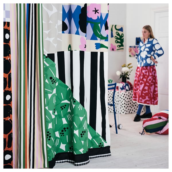 Vibrant room with colourful, patterned curtains and textiles. Person in blue and white polka-dot dress, holding red fabric.