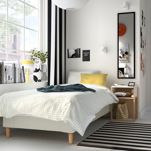Modern bedroom with white bed, striped rug, lamp, minimal decor.