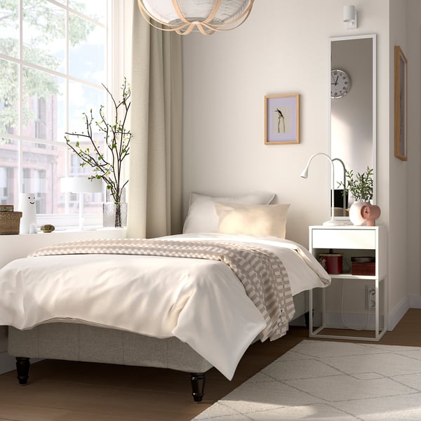 Minimalist bedroom with white bed, wooden floor, large window, small plant, and horizontal art.
