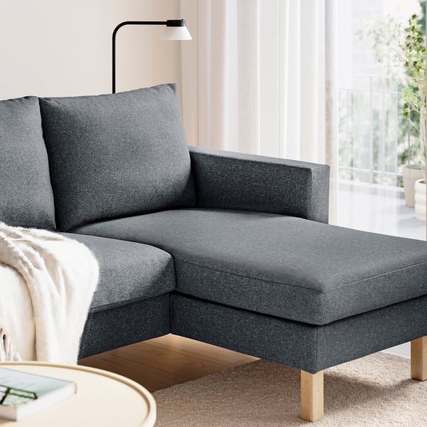 Dark grey sofa with chaise lounge, cushions, and wooden legs, positioned near a window.