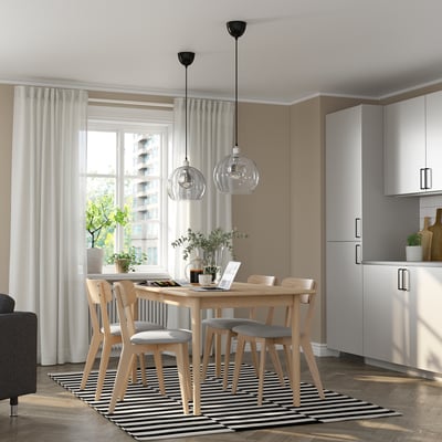Modern dining area with extendable table, chairs, and pendant lights near a large window.
