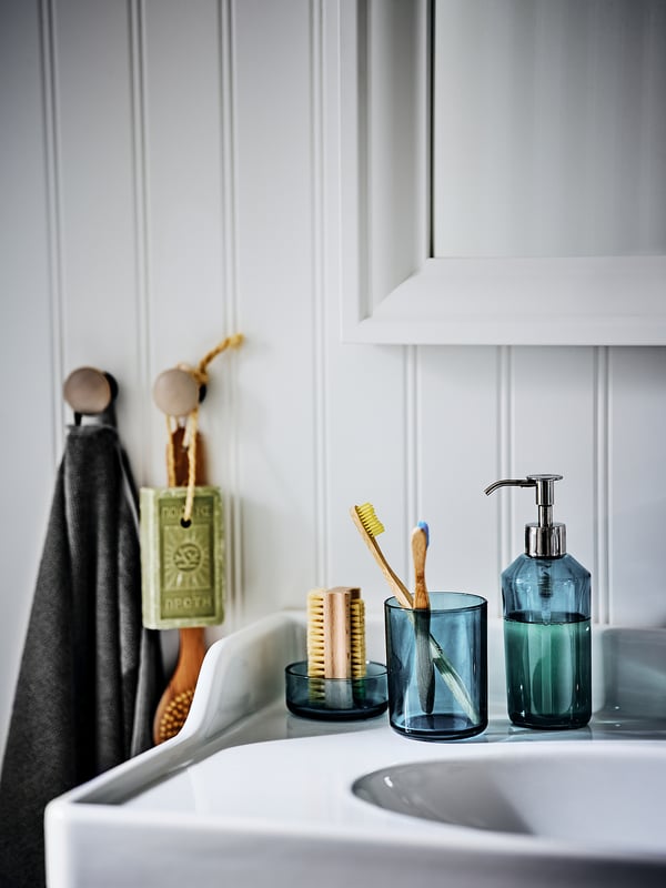 Modern bathroom with white sink, teal soap dispenser & toothbrush holder, grey towel on hooks.