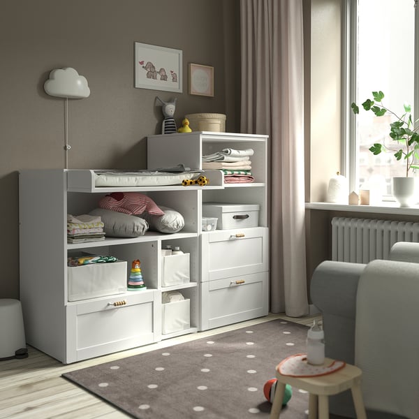Modern kids room with SMÅSTAD storage, changing table, toys, and grey chair by window.
