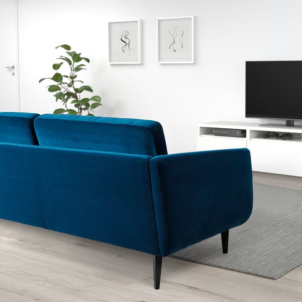 A modern living room with a blue velvet SMEDSTORP sofa, a television, and wall art. The sofa soft shapes, comfortable armrests, and cone-shaped legs.