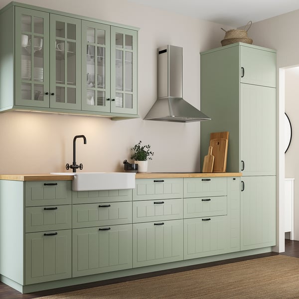 Modern kitchen with light green cabinets, wooden countertop, stainless tap, and range hood.