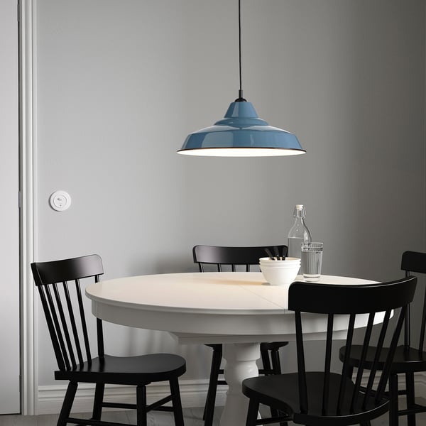 White dining table with black chairs, large blue lamp above, grey wall background.
