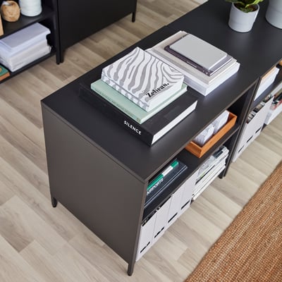 Black troffen cabinet with sliding doors dividing space, on wood floor, holding books, tray.