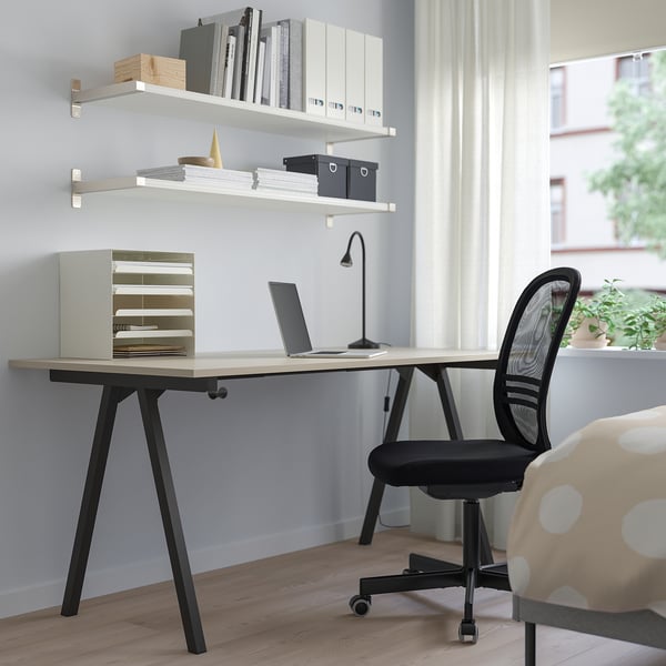 Beige TROTTEN desk with black legs, under white shelves, black chair, window, plant.