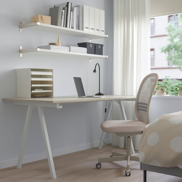 Minimalist home office with TROTTEN beige desk, wooden floor, shelves, lamp, laptop, tan chair, window.