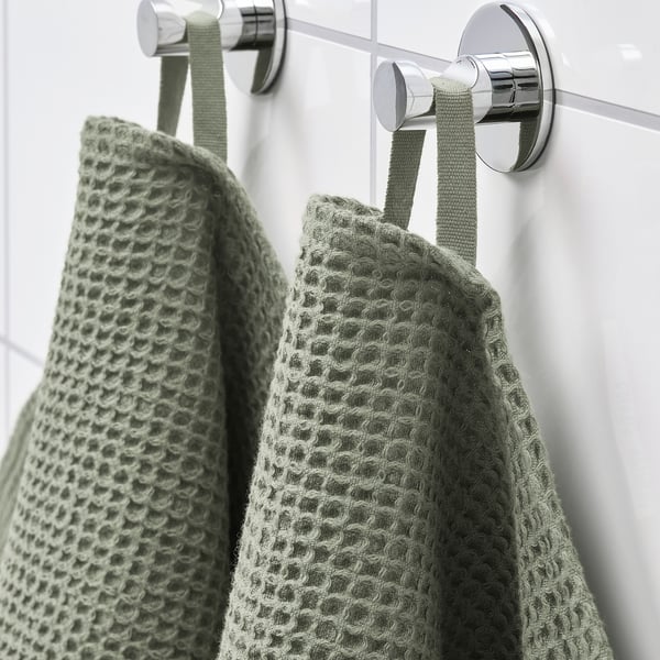 Two green towels hang on chrome hooks, showcasing absorbency and quick drying.