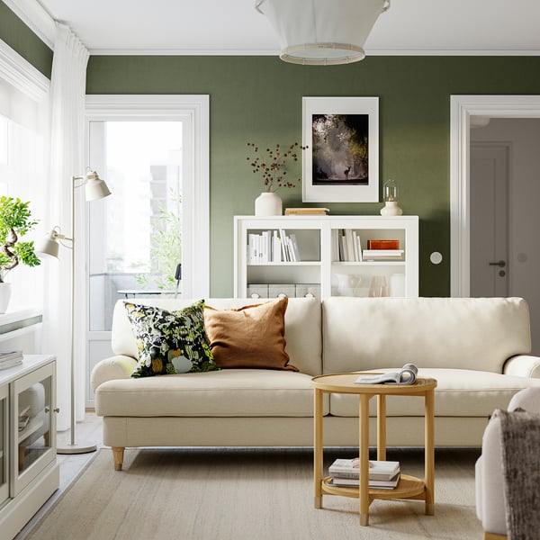 Cosy living room with cream sofa, brass feet, olive-green walls, fireplace, and coffee table holding books.