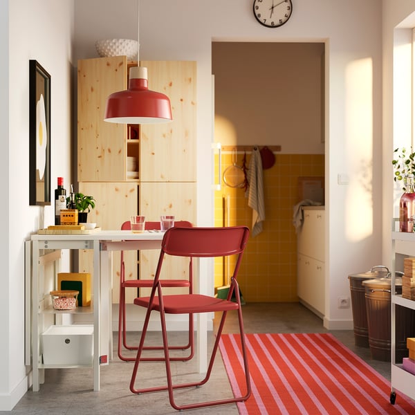 Modern living room with white gateleg table, red chairs, yellow kitchen in background.