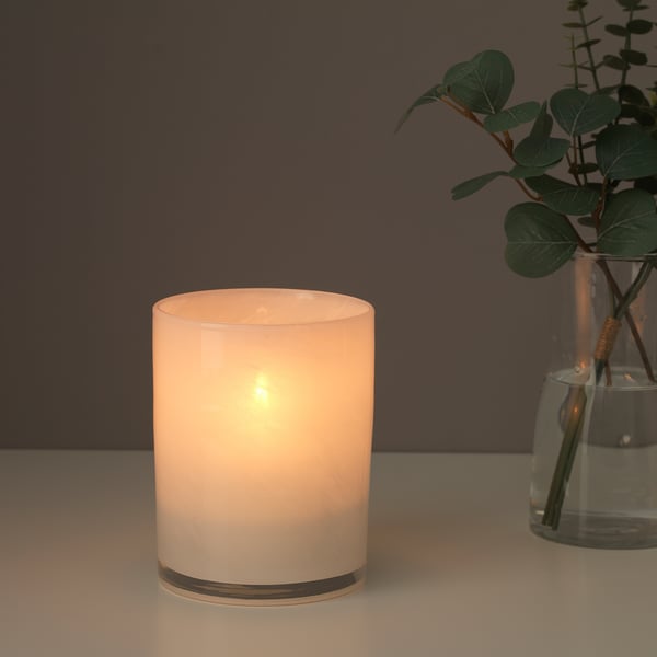 Cylindrical glass candle holder with frosted, golden base. Holds lit candle, emitting warm, soft light. Groups with green plant in clear vase.