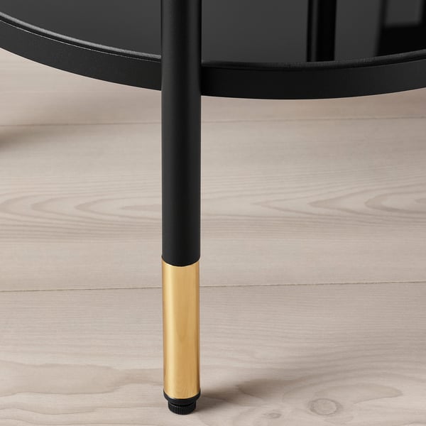 Close-up of modern round table leg with gold base, black metal and glass top, showcasing elegant design.