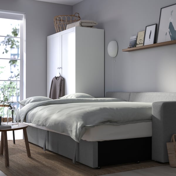 Minimalist bedroom with grey sofa-bed, flowers, and large window.