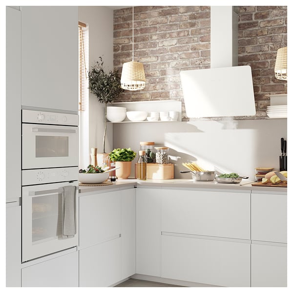Modern white kitchen with stainless steel oven, brick backsplash, open shelves with dishes, and hanging lamps.