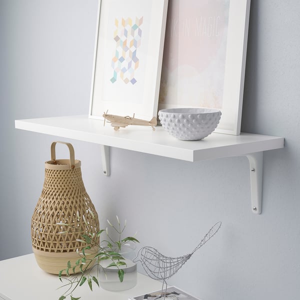 A white wall shelf displays a textured bowl, an abstract aeroplane, and two woven baskets, supported by white brackets.