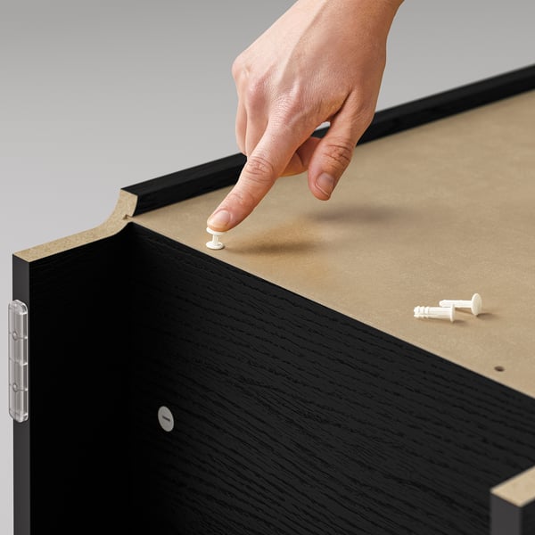 A hand placing a pushpin on a corkboard, securing a black BILLY bookcase.