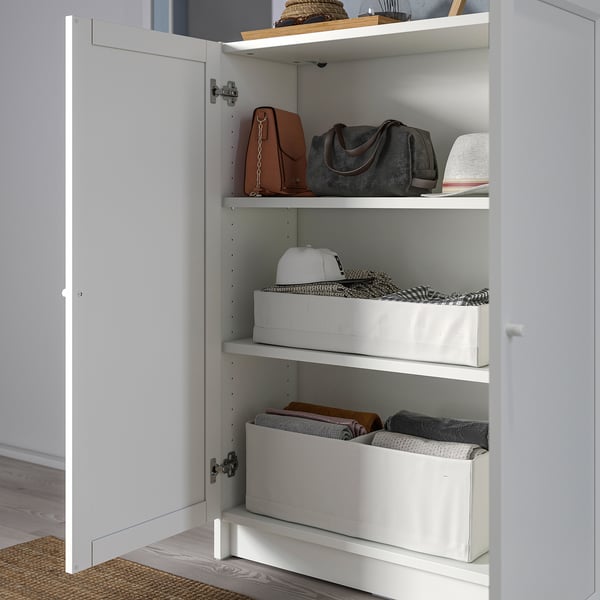 Open white BILLY bookcase with shelves holding folded clothes in boxes, handbags, and accessories.