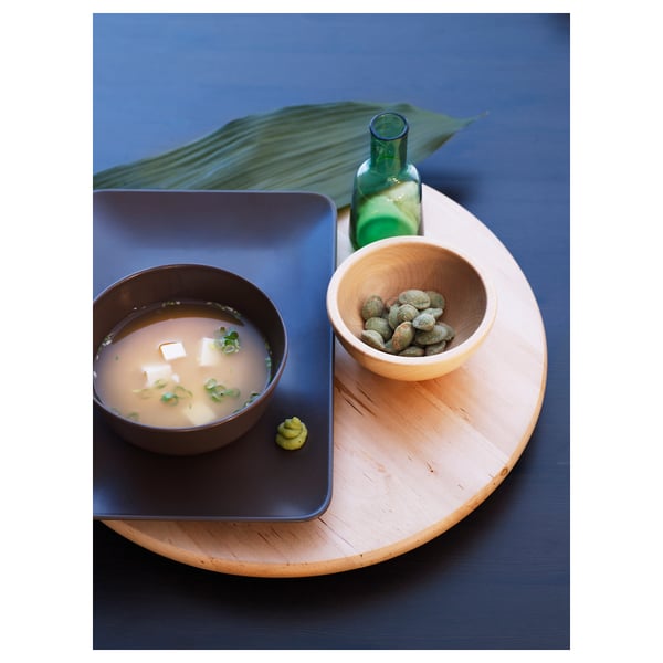 A wooden tray holds a blue bowl of soup and a bowl of green sweets, with a green bottle beside.