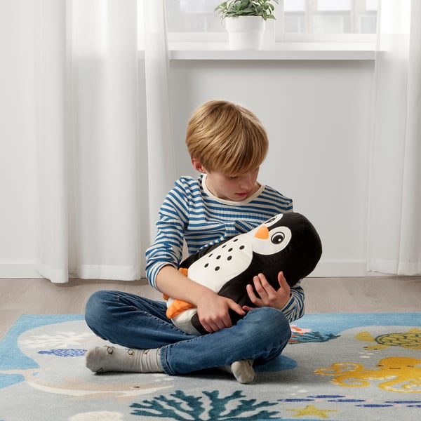 Boy hugging a plush penguin toy while sitting on a rug.