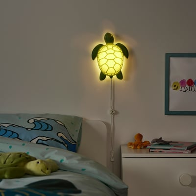 Turtle-shaped kids wall lamp emits soft light, ideal as a night-light. Mounted near a bed with ocean-themed decor.