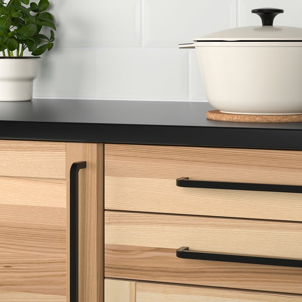 Modern kitchen drawers with light wood, black handles, and a plant.
