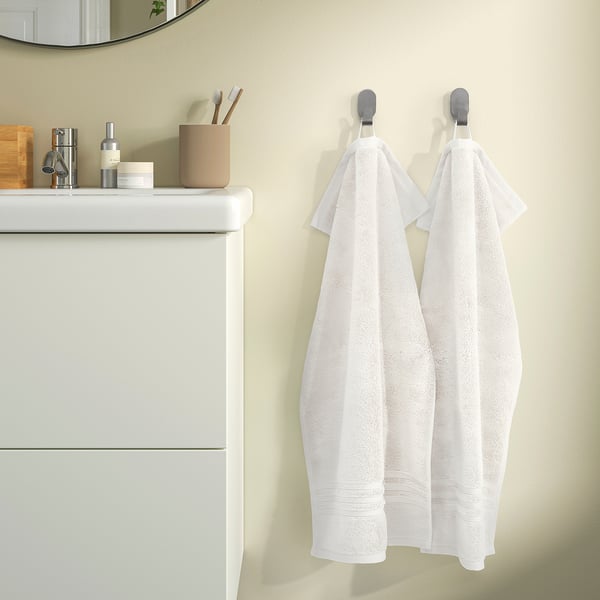 Two white towels hang on hooks beside a white vanity with a beige countertop.