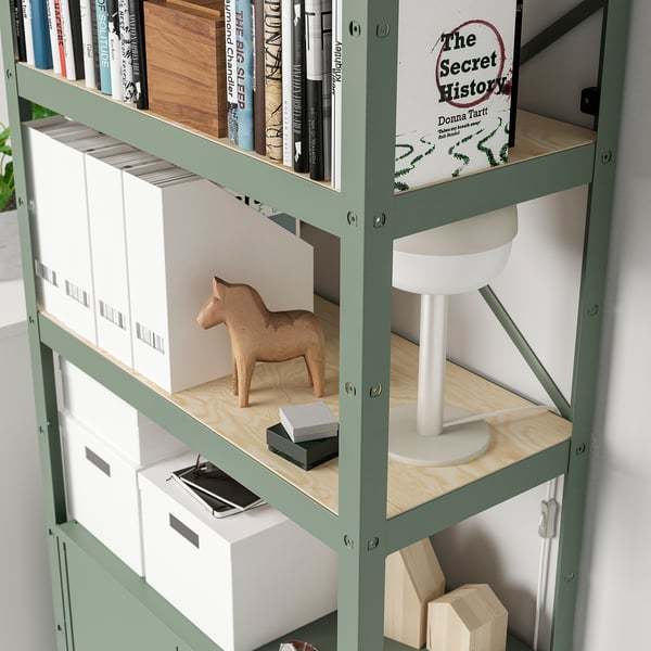 Green metal shelf with books, boxes, wooden horse, and lamp. Sturdy, heavy-duty storage.