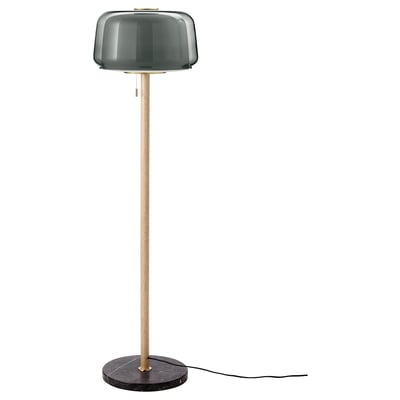 An EVEDAL floor lamp with a dark green glass shade, brass accents, and a marble base. It combines scandinavian design with modern materials.