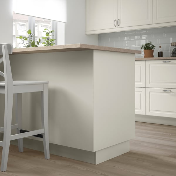 Modern kitchen island with FÖRBÄTTRA counter. White colour, wooden floors. Countertop has potted plants, chairs nearby.