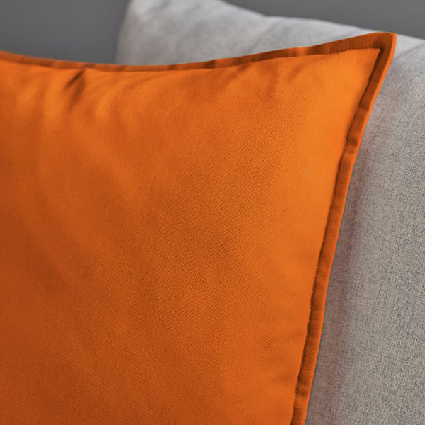 Bright orange cushion resting on a textured grey surface. High-quality cotton fabric, neatly stitched with a visible zip.