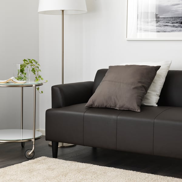 Dark brown sofa with cushions and a lamp beside it on a side table with a plant.