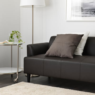 Dark brown sofa with cushions and a lamp beside it on a side table with a plant.
