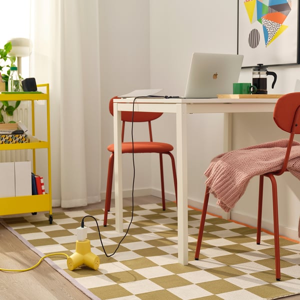 Home office with desk, laptop, coffee maker, orange chairs, yellow cord, and plant cart.