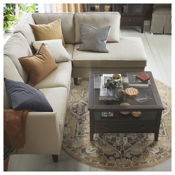 Modern living room with beige sectional, pillows, coffee table books, and patterned rug.