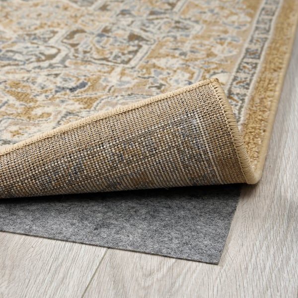Decorative beige and grey rug folded back to reveal durable, non-slip backing, lying on wooden floor.